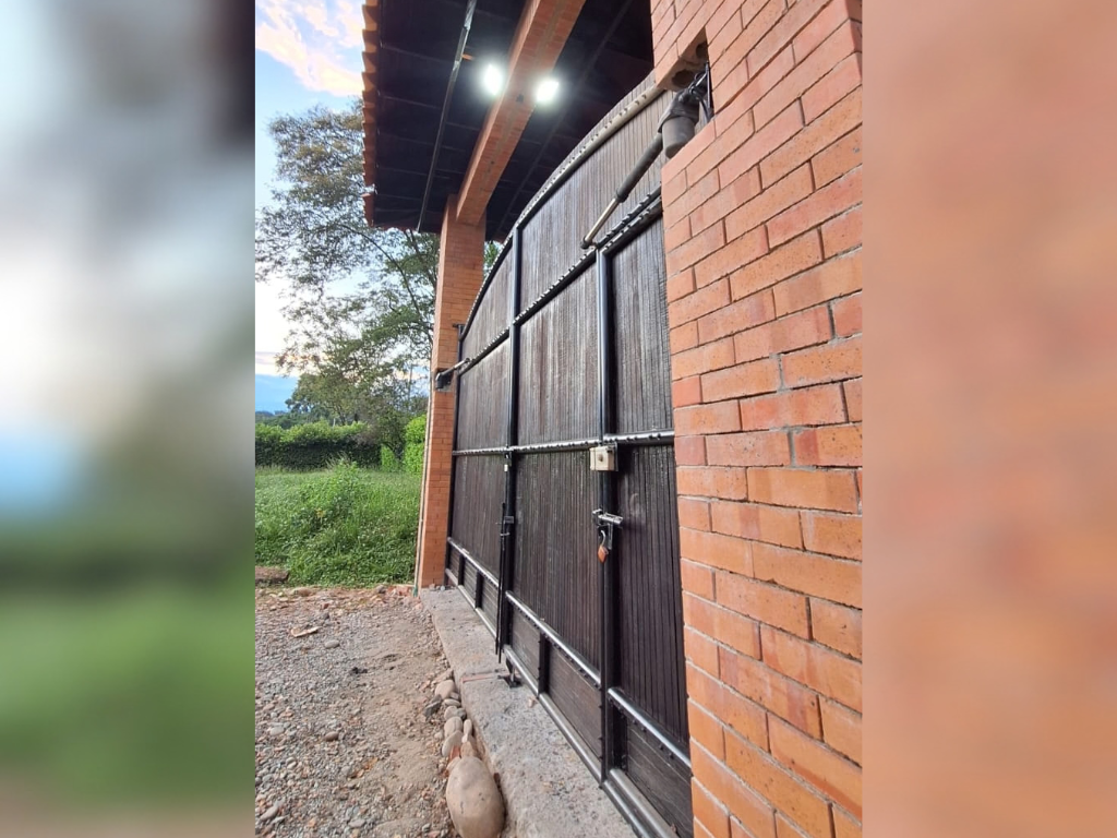 Puerta batiente oscura automatizada con brazo mecánico, instalada en una estructura de ladrillo