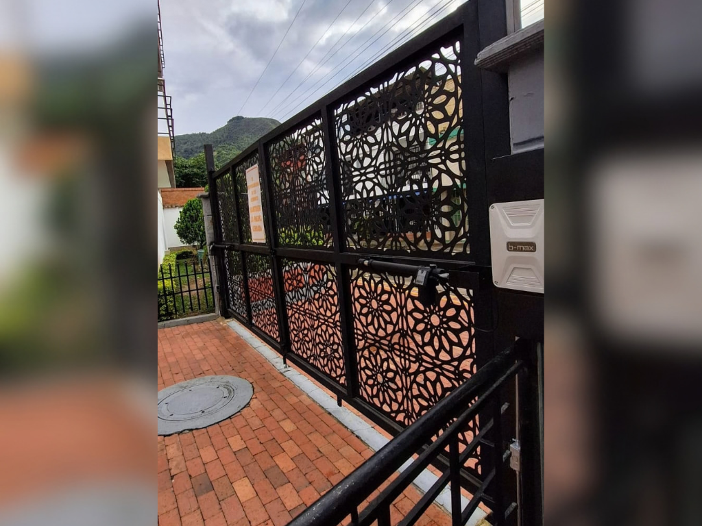 Puerta batiente automatizada con paneles decorativos de metal en corte láser y motor B-max