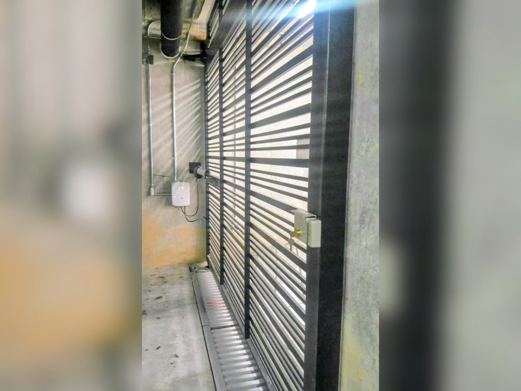Puerta corredera de rejilla metálica instalada en un garaje subterráneo de concreto con caja de motor en la pared