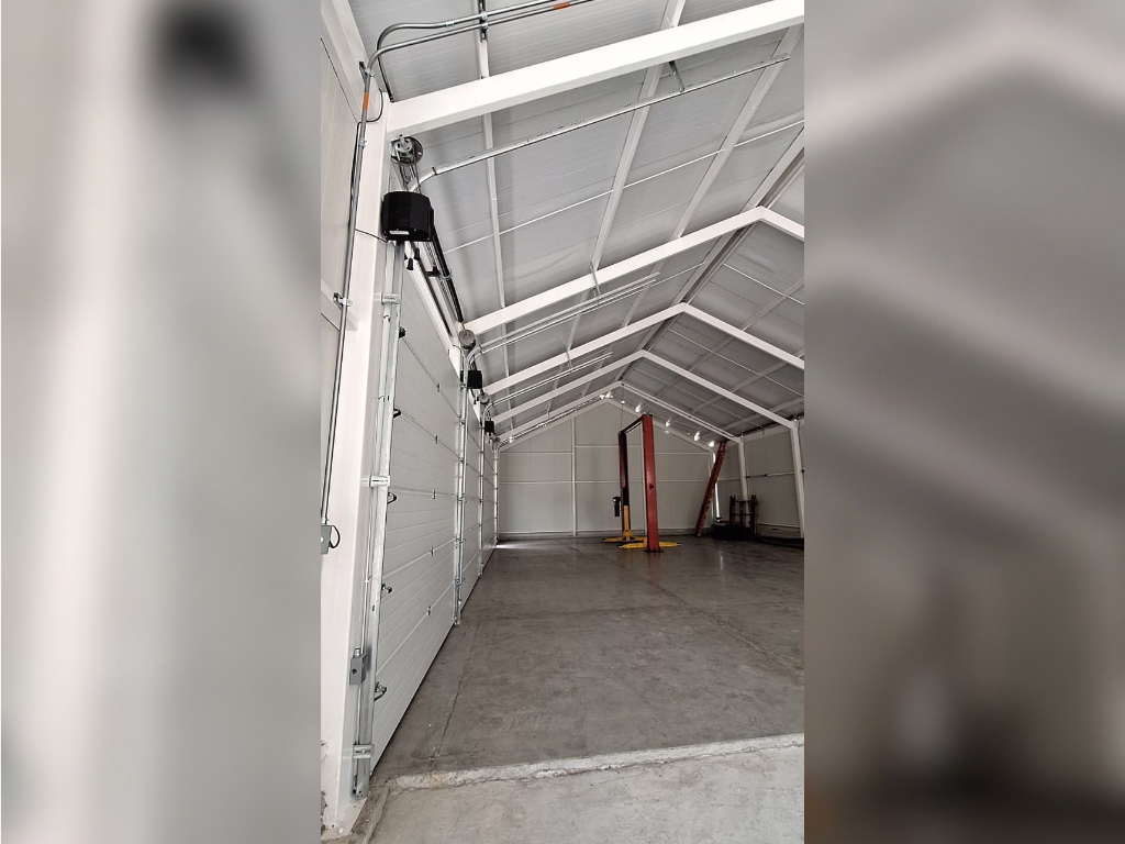 Puerta seccional blanca de gran tamaño instalada con rieles y motor en el interior de una bodega industrial